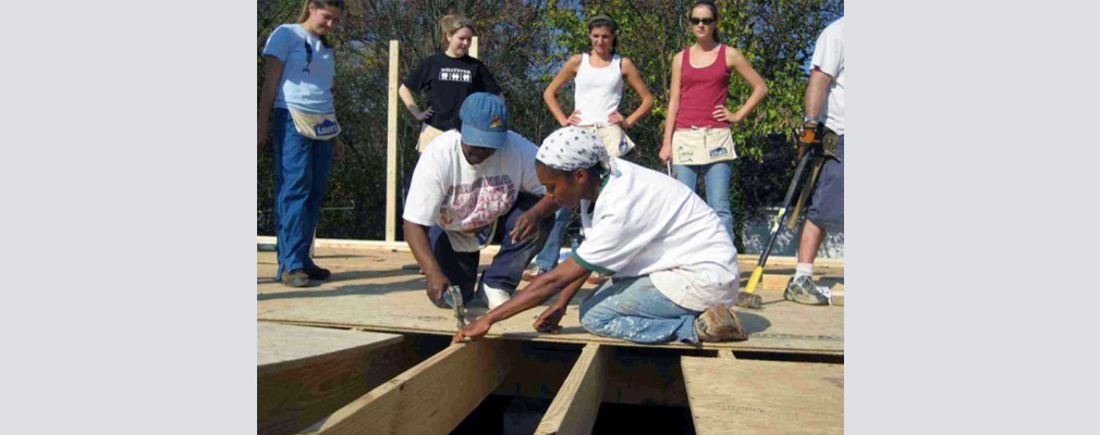 Photograph of seven volunteers laying plywood for the subfloor of a house.