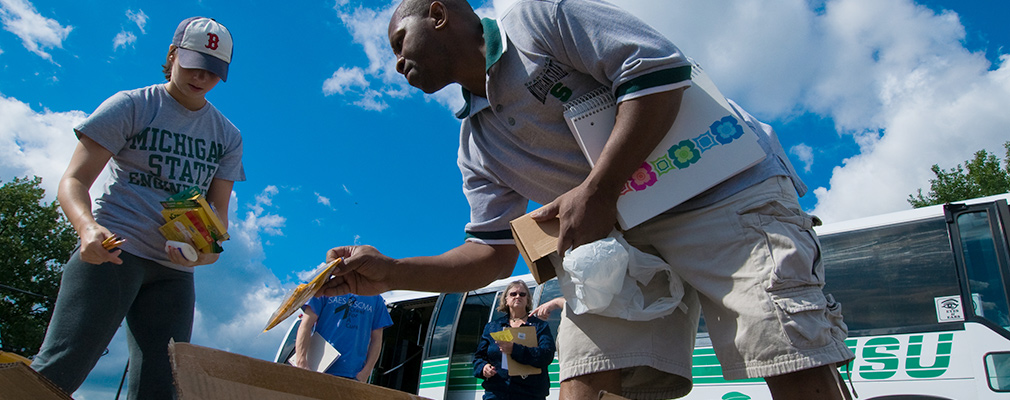 Photograph of two university students sorting school supplies in front of an MSU bus.