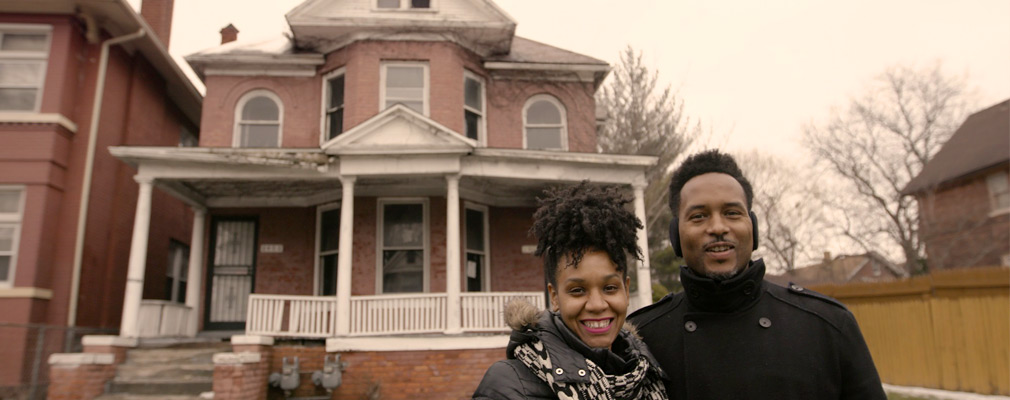 Photograph of a man and a woman standing in front of a two-story brick single-family house.