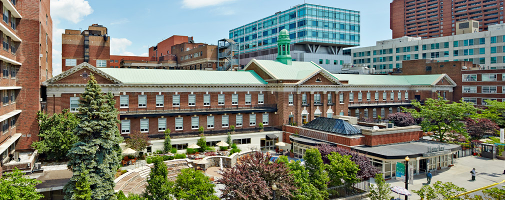 Photograph taken several stories above street level of the Moses medical campus, a cluster of modern and historic buildings around a central, tree-lined courtyard.