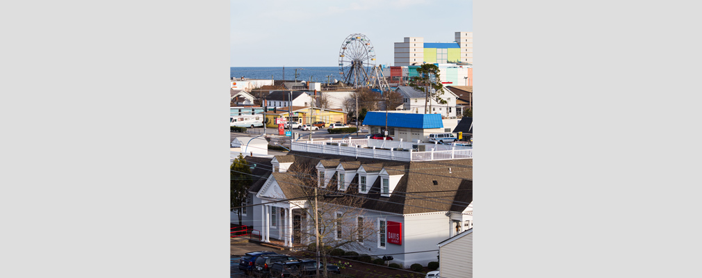 Photograph taken from an apartment balcony of buildings and a Ferris wheel located between Seaside Harbor and the Atlantic Ocean. 
