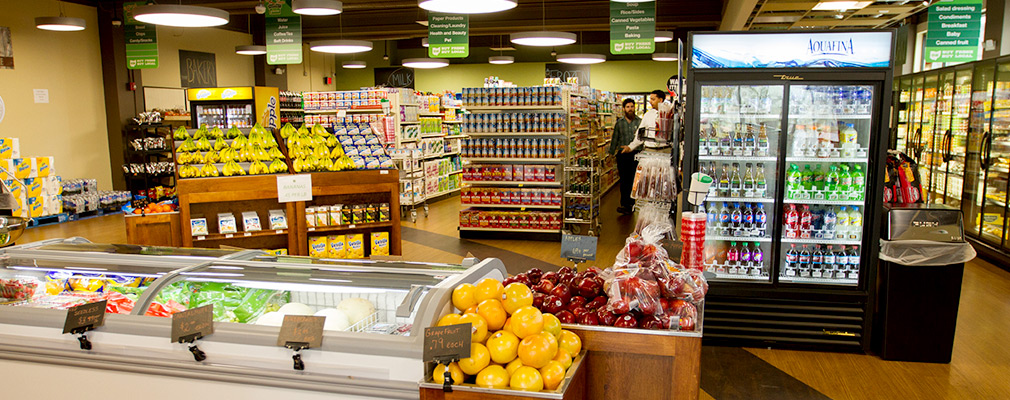 Photograph of the produce section of a grocery store, with other food items on shelves in the background.
