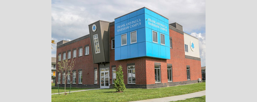 Photograph of two façades of a brick two-story building, with a wall sign reading “Frank and Paula Harshaw Campus” on each wall.