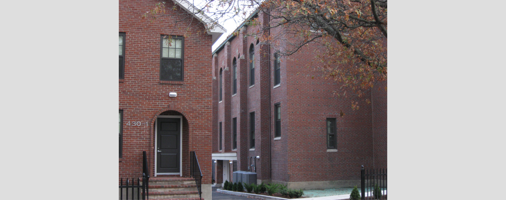 Photograph of portions of the front façade of two brick buildings, a rectory on the left and a church on the right.