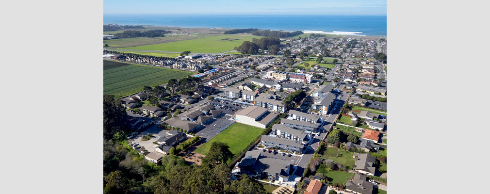 Low-angle aerial photograph of a portion of the city of Half Moon Bay, with the senior campus behind and to the right of the large school building near the center of the photograph and the Pacific Ocean in the background.