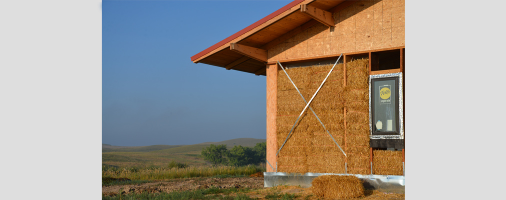 Photograph of an unenclosed wall of a straw bale building, with South Dakota’s rolling hills in the background.
