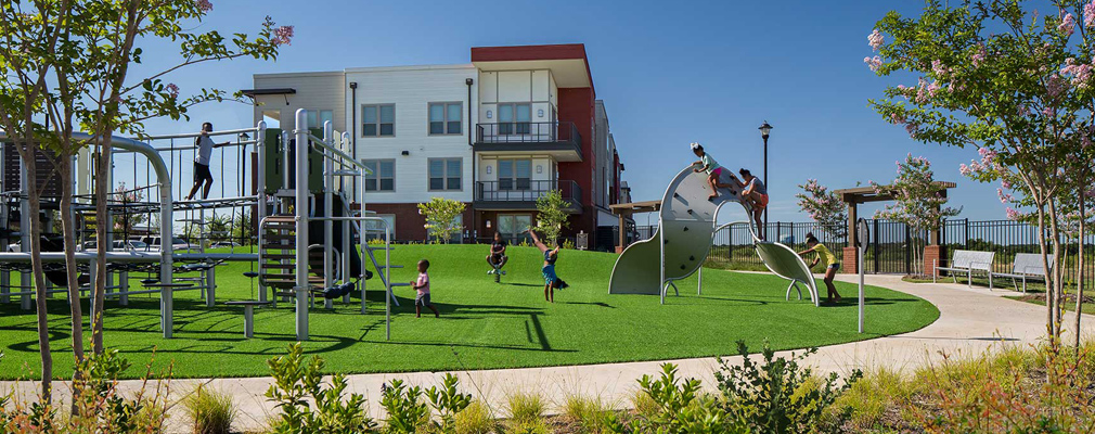 Photograph of children at a playground, with an apartment building in the background.