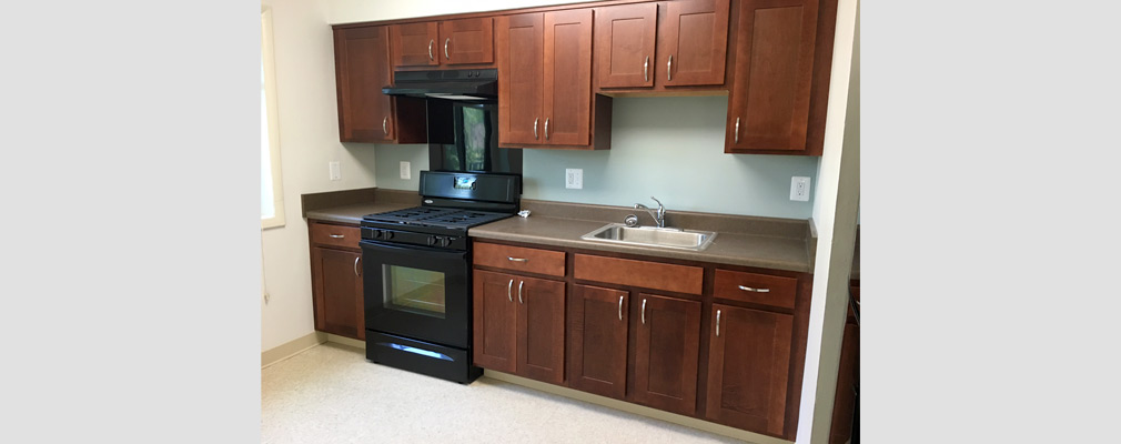 Photograph of a kitchen with a sink, oven, and upper and lower cabinets.