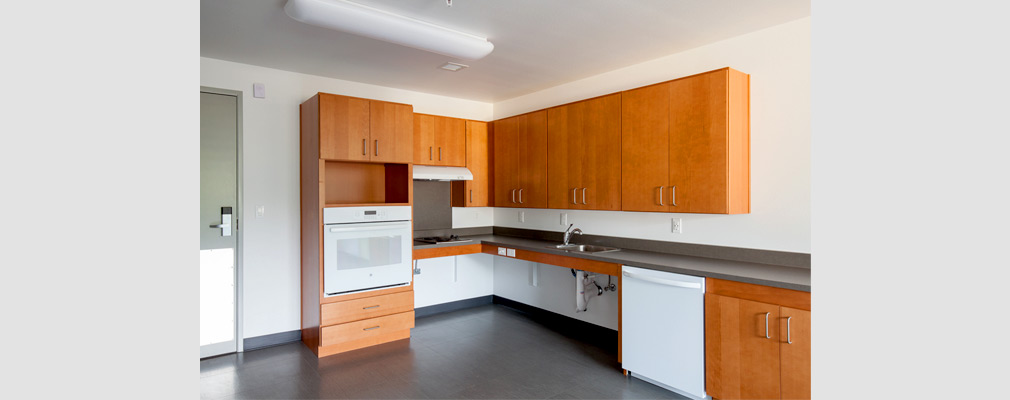 Photograph of a kitchen with an oven, stovetop, sink, dishwasher, roll-under counter space, and cabinets.
