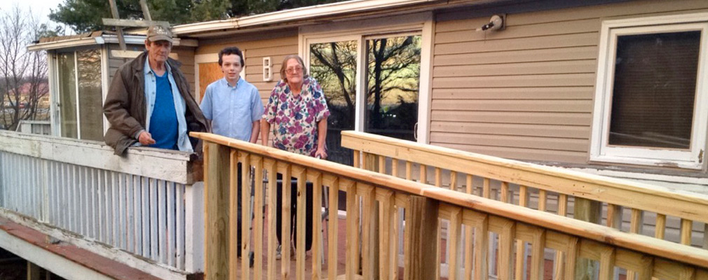 Photograph of three residents standing on their front porch at the top of a newly constructed ramp. 