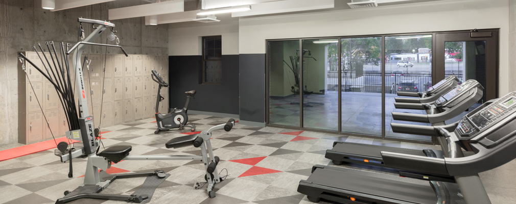 Photograph of a large room with three treadmills, other exercise equipment, and lockers along a side wall.