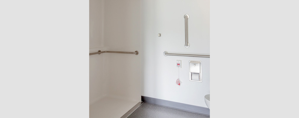 Photograph of a bathroom with a wide, roll-in shower; handrails on the walls; and wide separation between a toilet and the shower.