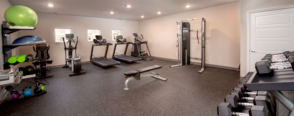 Photograph of an exercise room furnished with dumbbells, a functional trainer, and aerobic equipment.
