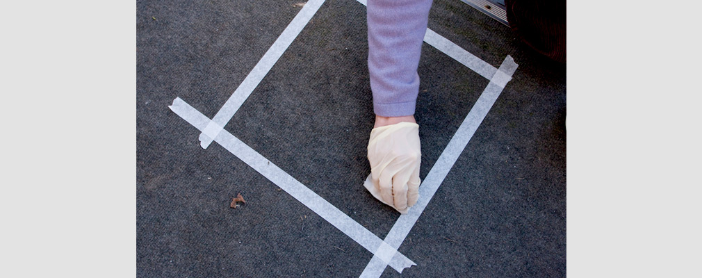 Photograph of a gloved hand wiping a cloth within a taped square on a floor.