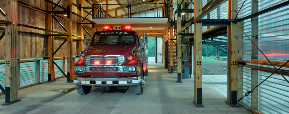 Photograph of a fire truck parked inside a modern fire station.