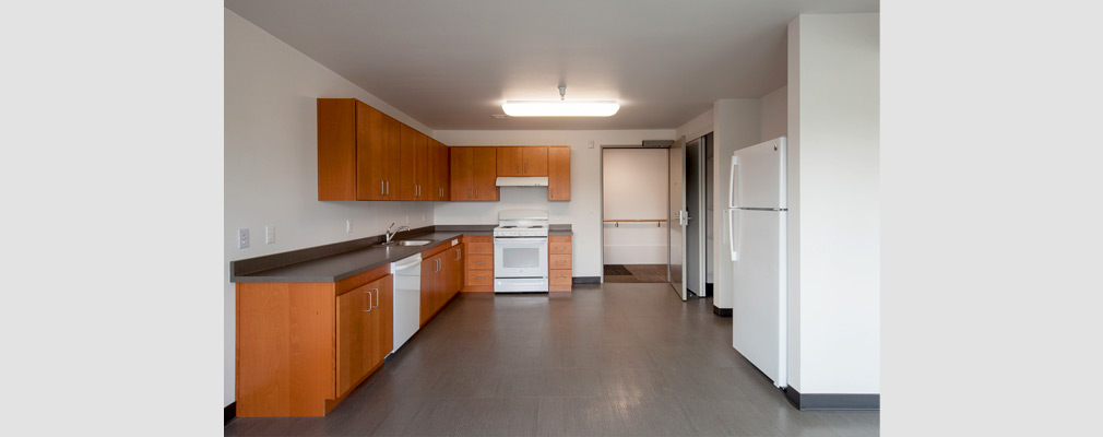 Photograph of a kitchen with clear floor-space for maneuvering, a wide door, appliances, and cabinets. 