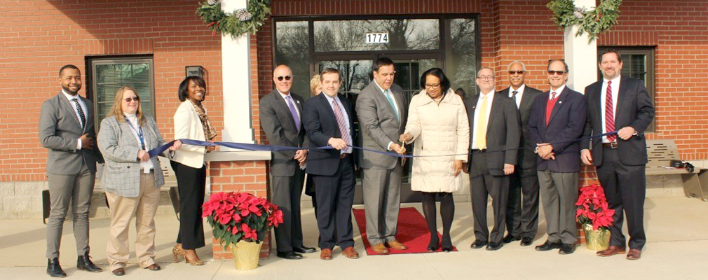 Photograph of a dozen men and women at a ribbon cutting in front of an entrance to Fairwood Commons.