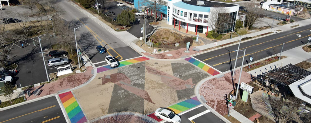 Low-angle aerial photograph of a four-way street intersection with crosswalks painted with the LGBTQ rainbow.
