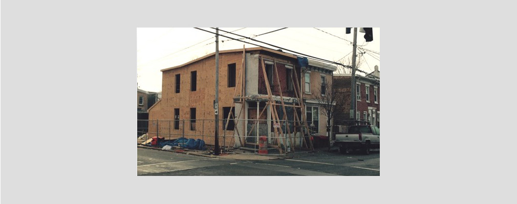 Photograph of a two-story rowhouse under construction on a corner lot.