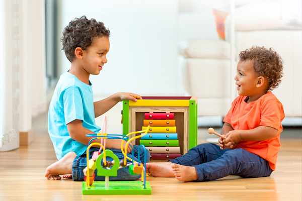 Two young children sit across from each other and play with a wooden toy. 