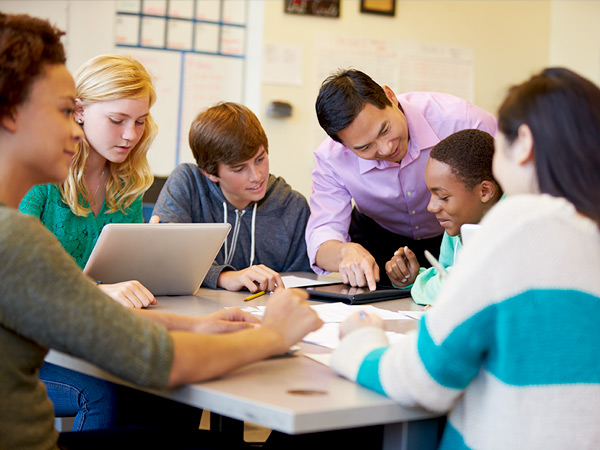 Image of teacher assisting six students in a classroom.