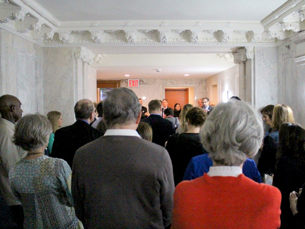 Photograph of approximately two dozen neighbors, residents, and other interested people standing in an ornate marble lobby during the ribbon-cutting ceremony.