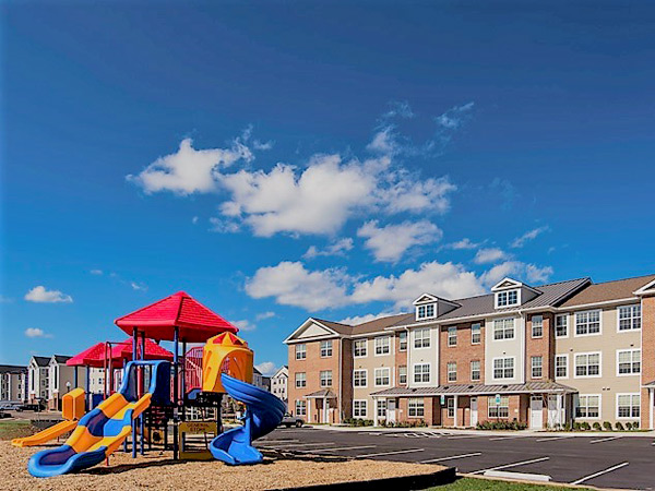 Photograph of a three-story multifamily building with play equipment in the foreground.