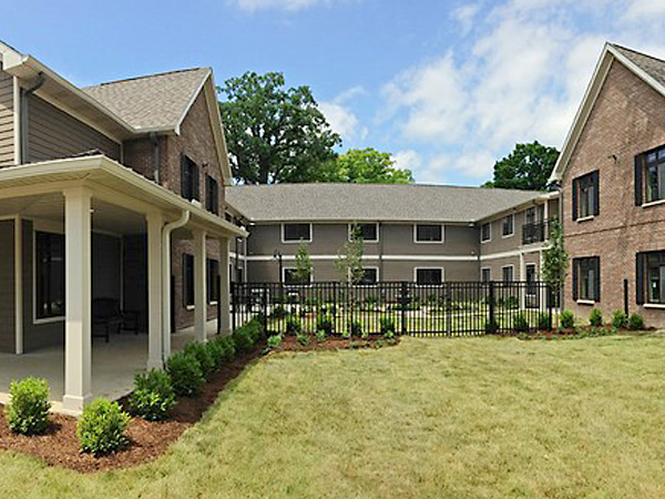 Photograph of a two-story residential building extending around three sides of a landscaped courtyard.