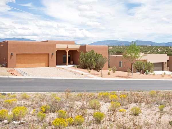 Photograph of two detached, flat-roofed Pueblo Revival houses with scrubland and mountains in the background.