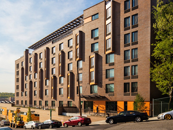 Image of a multi-story brick residential building along a sloped street.