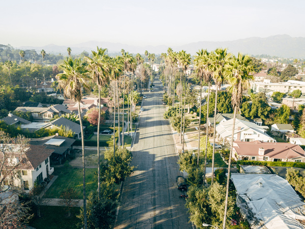 An aerial photograph of a neighborhood of single family homes along a street lined with palm trees.