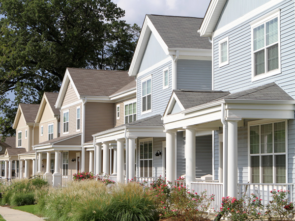 A row of multistory townhomes with front porches line a sidewalk.