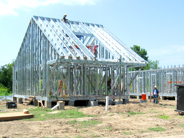 Photograph of workers constructing a steel frame of a home with a gable roof.