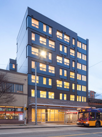 Photograph of the front façade of a seven-story apartment building, with storefront space on the first floor.