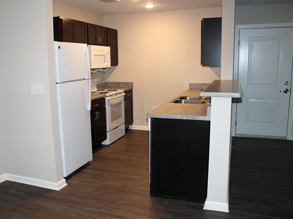 Image of apartment unit kitchen with white appliances, steel sink, and cabinets.