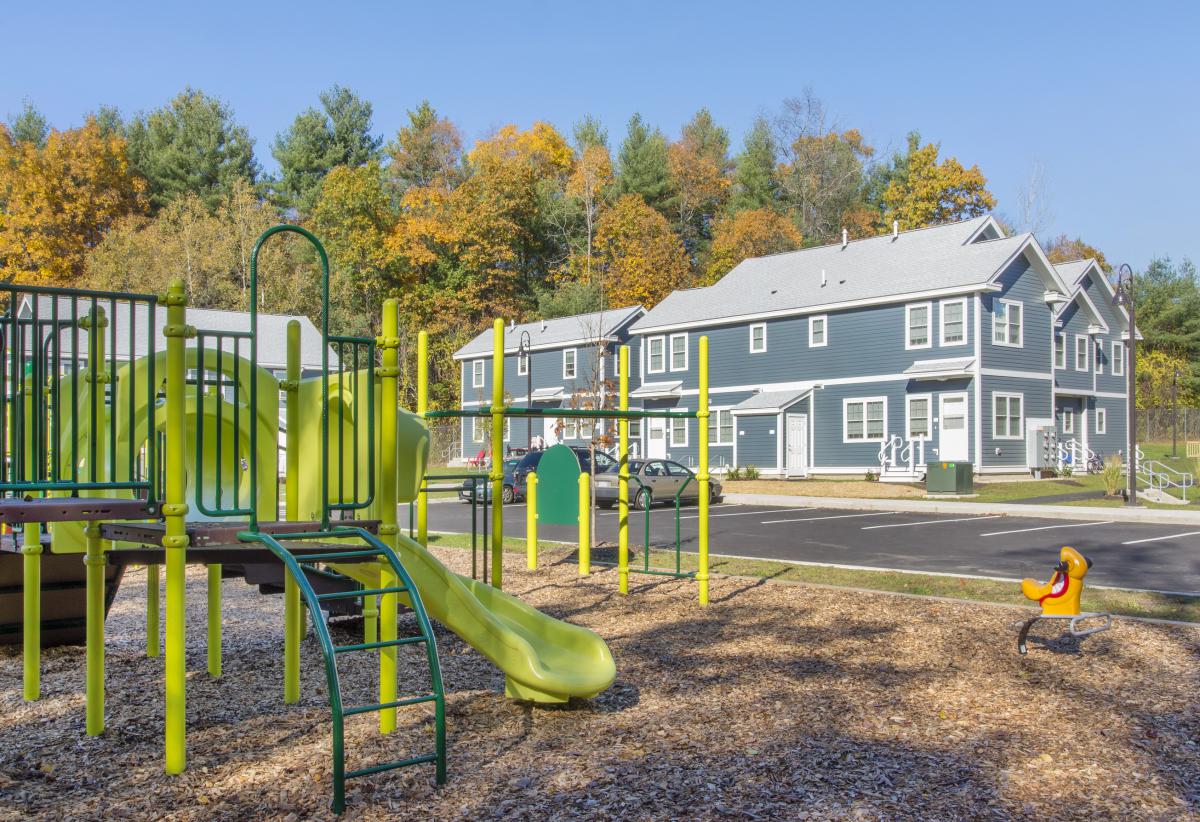 Image of two-story, colonial-style apartment buildings with playground structure in the foreground.