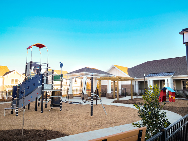 A residential outdoor playground complete with benches, picnic tables, shade areas, and plants.