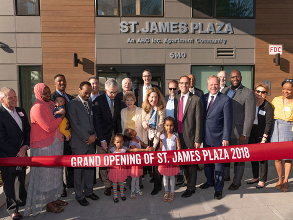 Photograph a group of people attending a ribbon-cutting ceremony for St. James Plaza.
