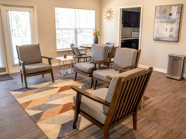 A community room with furniture, with sunshine through windows and artificial light filling the space.