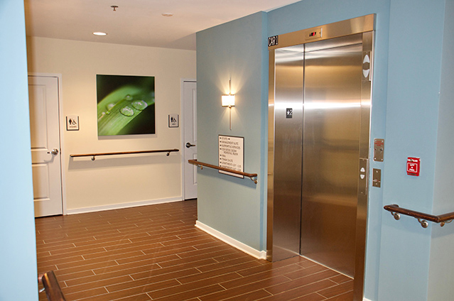 Picture of an apartment building hallway, showing an elevator, handrails along the walls, and handicap accessible bathrooms.