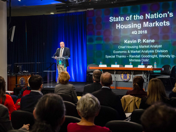 Image shows Kevin Kane speaking on a podium before an audience with a presentation slide titled State of the Nation’s Housing Markets on the screen behind him.