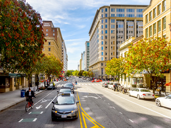 A photograph of a pedestrian-friendly, tree-lined streetscape with bike lanes alongside cars and buildings in the background. 