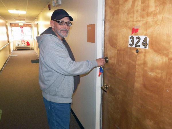 A person stands in a hallway unlocking an apartment door.