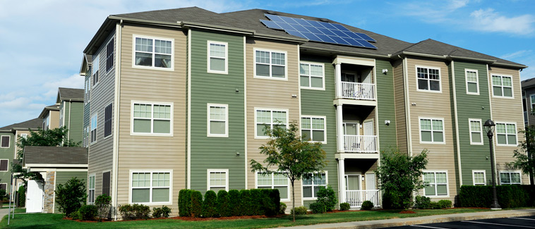Photograph of the rear façade of a three story multifamily residential building featuring solar panels on the roof.