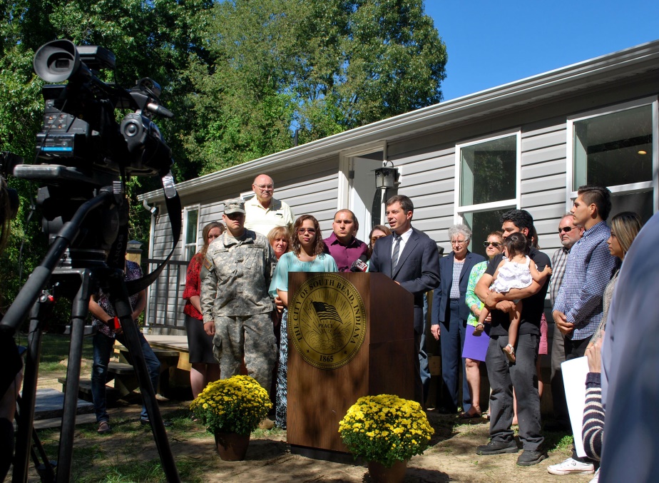 Photograph of approximately 15 people at a press conference in front of a rehabilitated house.
