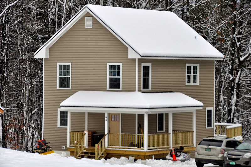Photograph of the font and side façades of a two-story, single-family detached house blanketed with snow. 