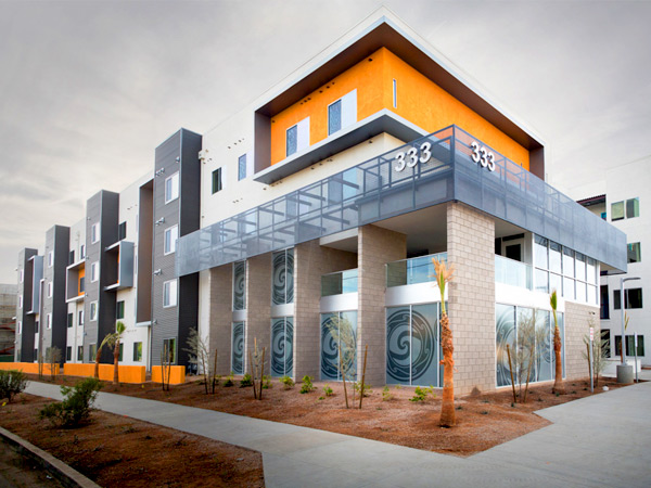 Photograph of the exterior of a 4-story apartment building with a sidewalk and desert landscaping in the foreground.