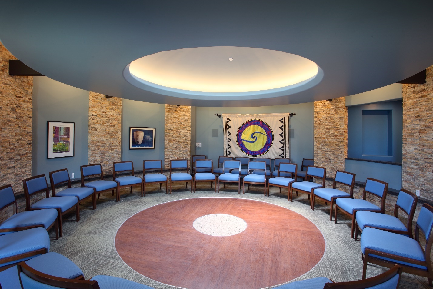 Photograph of the talking circle room at the Patina Wellness Center that has several chairs arranged in a circle with a skylight and Native American art.