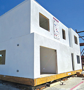 Photo shows two sides of an earthquake-resilient home with white walls and openings for doors and windows.