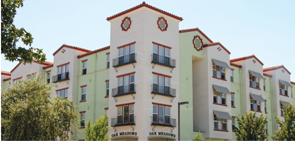 Photo shows two facades of a four-story multifamily building with two signs that read “Oak Meadows.” 